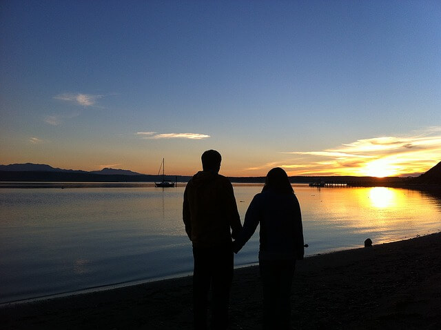 夕日の見える湖で手をつなぐカップル