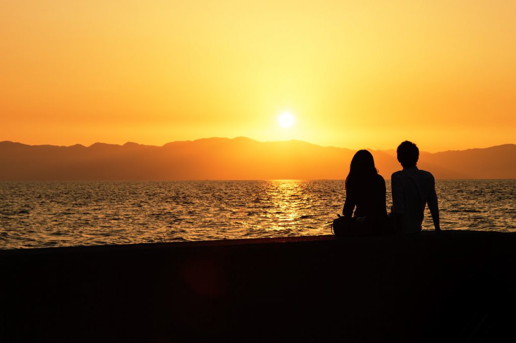 海岸で夕日を見るカップル