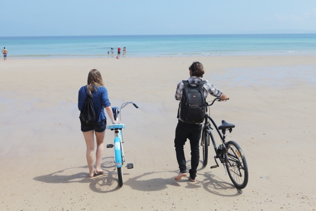 砂浜で自転車を持って歩くカップル