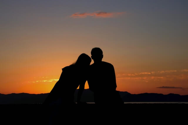 海沿いに腰かけて夕日を見るカップル